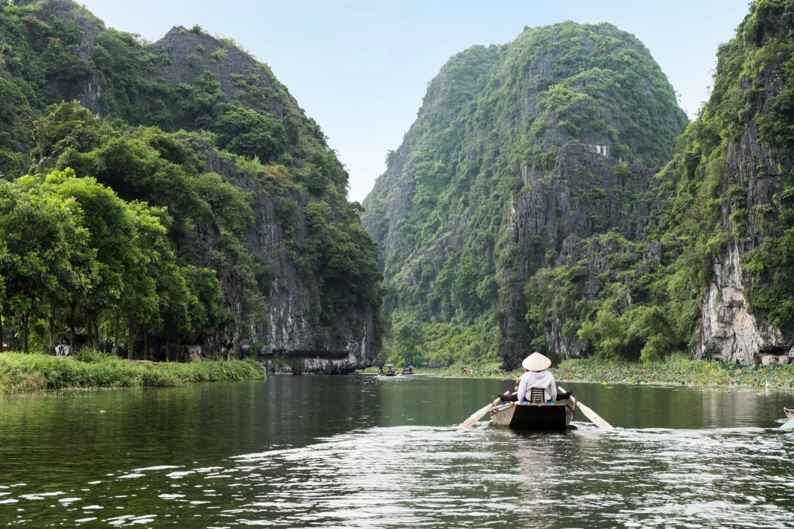 Rowboat with a conical-hat rower on a river among limestone mountains