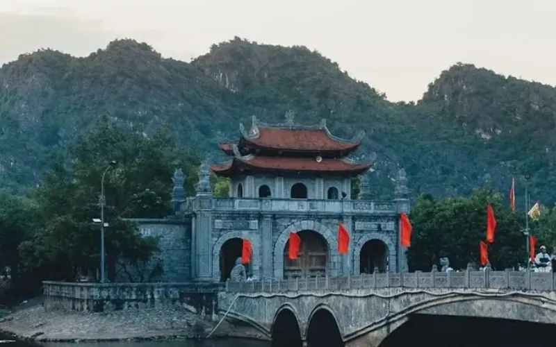 Stone gatehouse of the ancient capital Hoa Lu with red flags and mountains behind