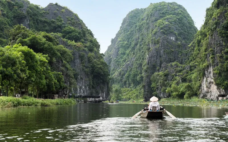 Rowboat carrying visitors between limestone cliffs on the Trang An river in Ninh Binh